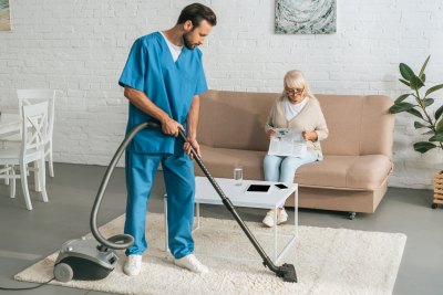 caregiver cleaning carpet while senior woman reading newspaper